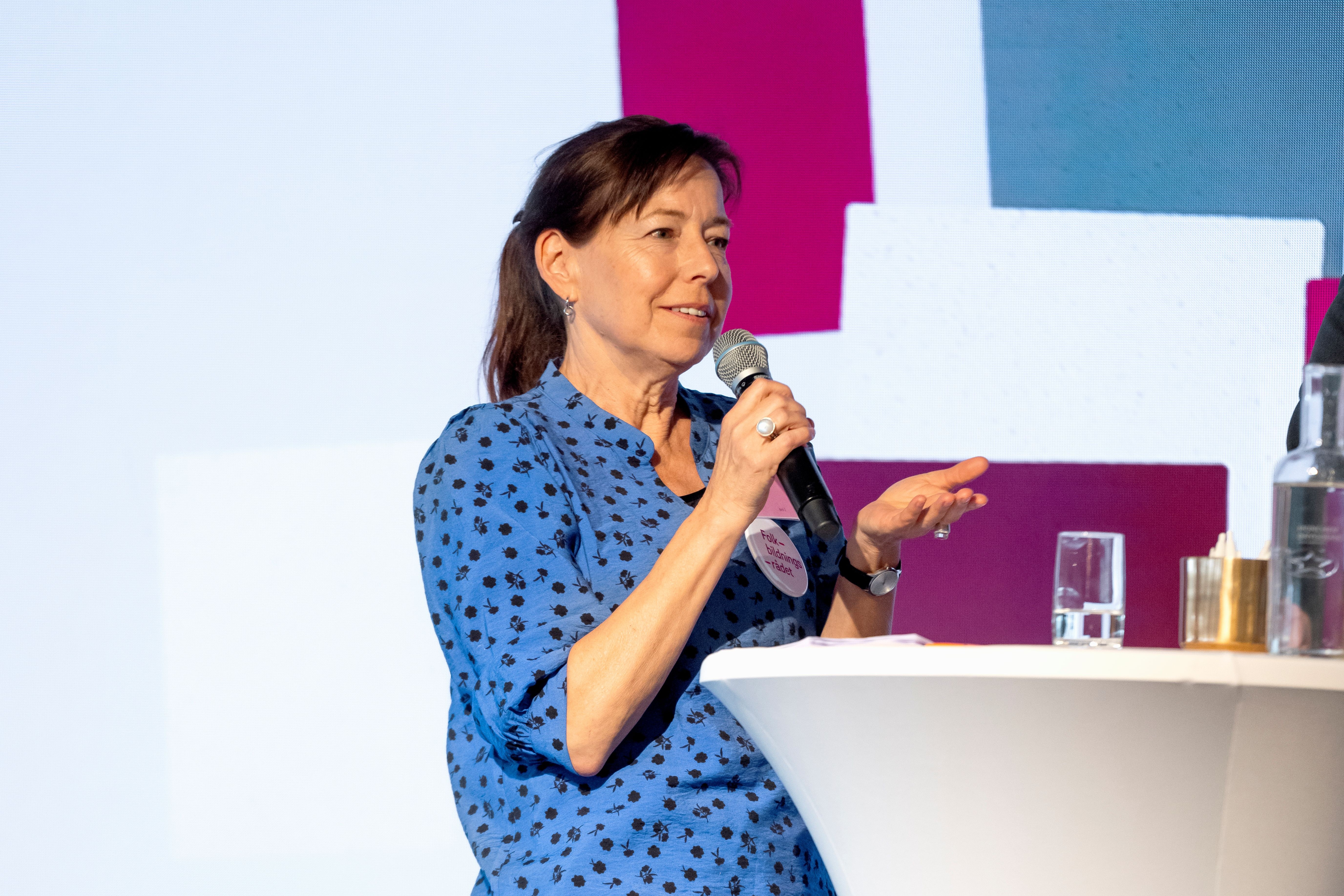 Anna-Karin Lindblom står på scen och pratar. Hon har en blå blus med svarta prickar på sig.