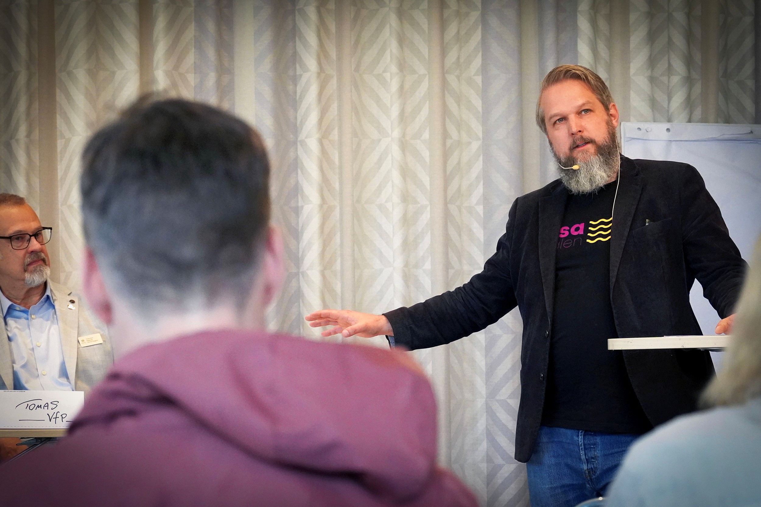 Daniel Berton står och håller en presentation, han är iklädd kavaj och en tröja med Åsadalens logotyp.