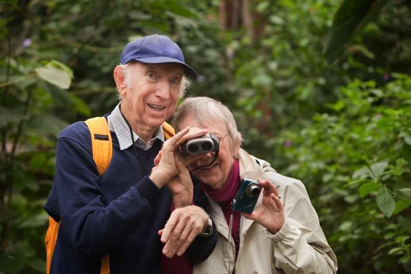 Äldre par i skogen. En man hjälper en kvinna att titta i en kikare.