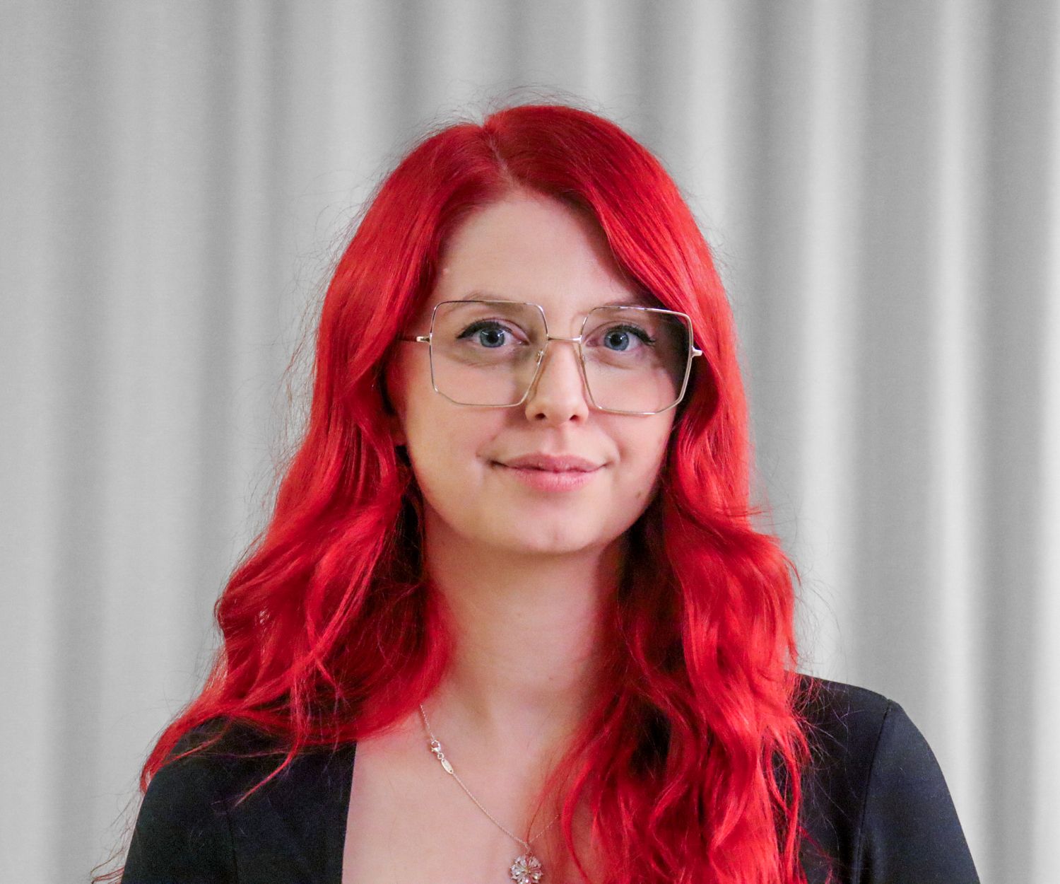 Porträttfoto av Julia Olsson Grunnan. Julia har glasögon, svart tröja och rött hår.