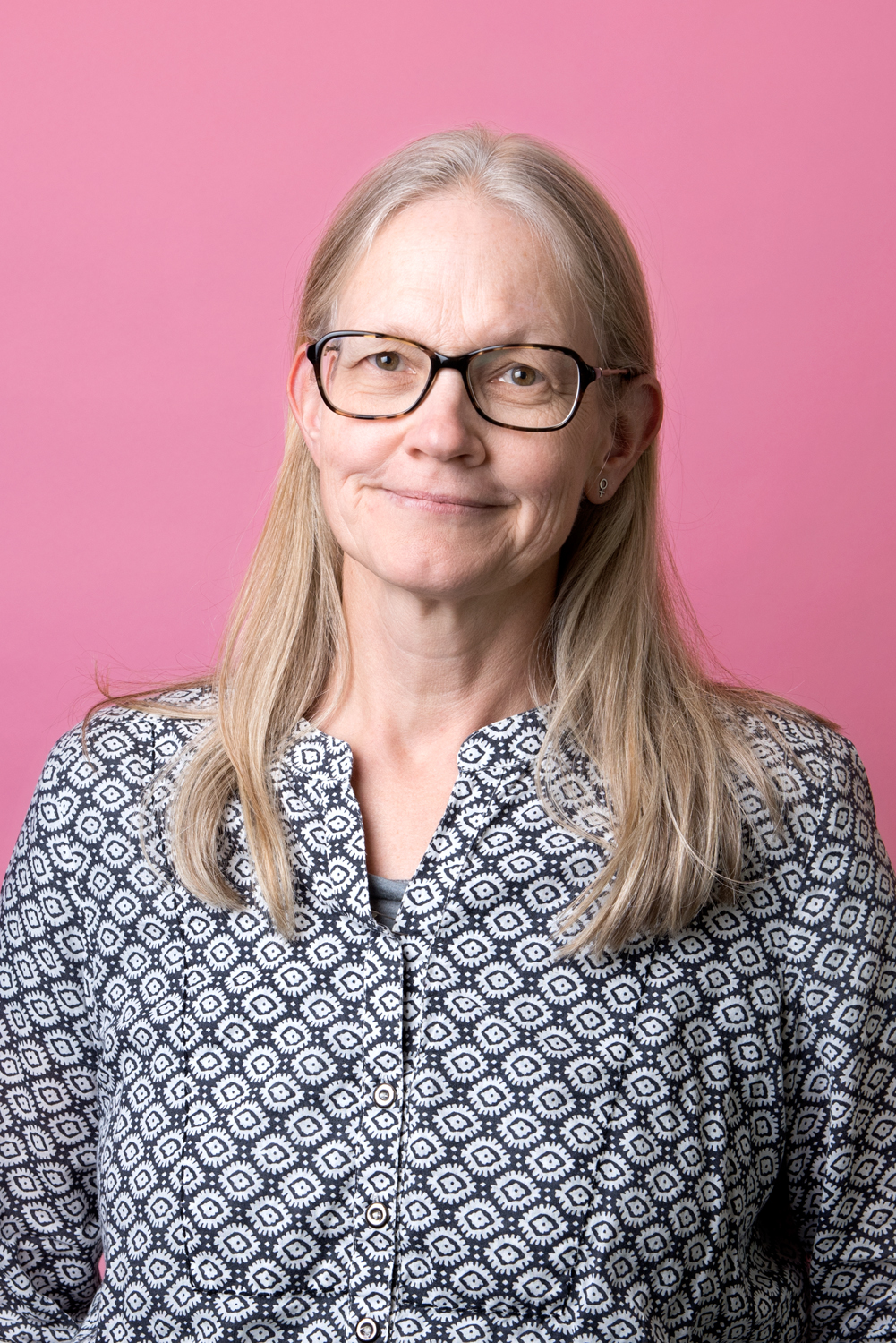 Porträttbild Karin Gustavsson. Karin har fyrkantiga glasögon och tittar rakt in i kameran. Hon bär en mönstrad blus i blått och vitt.