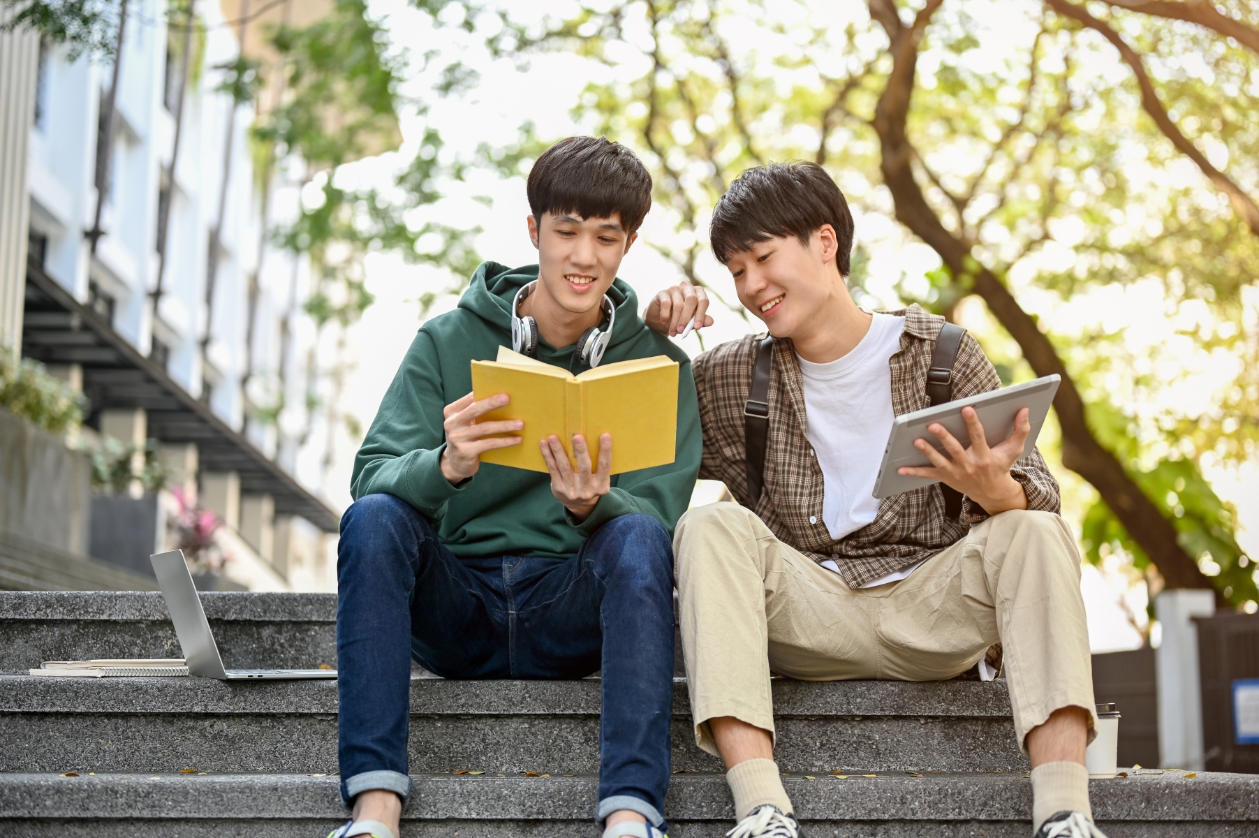 Två unga studenter sitter på en trappa och läser tillsammans i en bok.