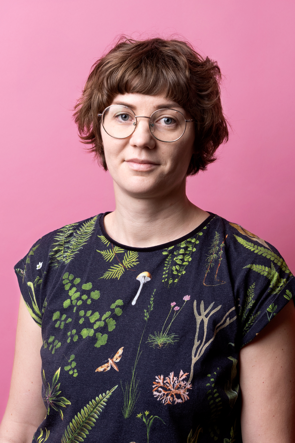 Porträttbild Josefina Linde. Josefina har runda glasögon och bär en mörk tröja med svampar, blad och andra skogsrelaterade saker på.