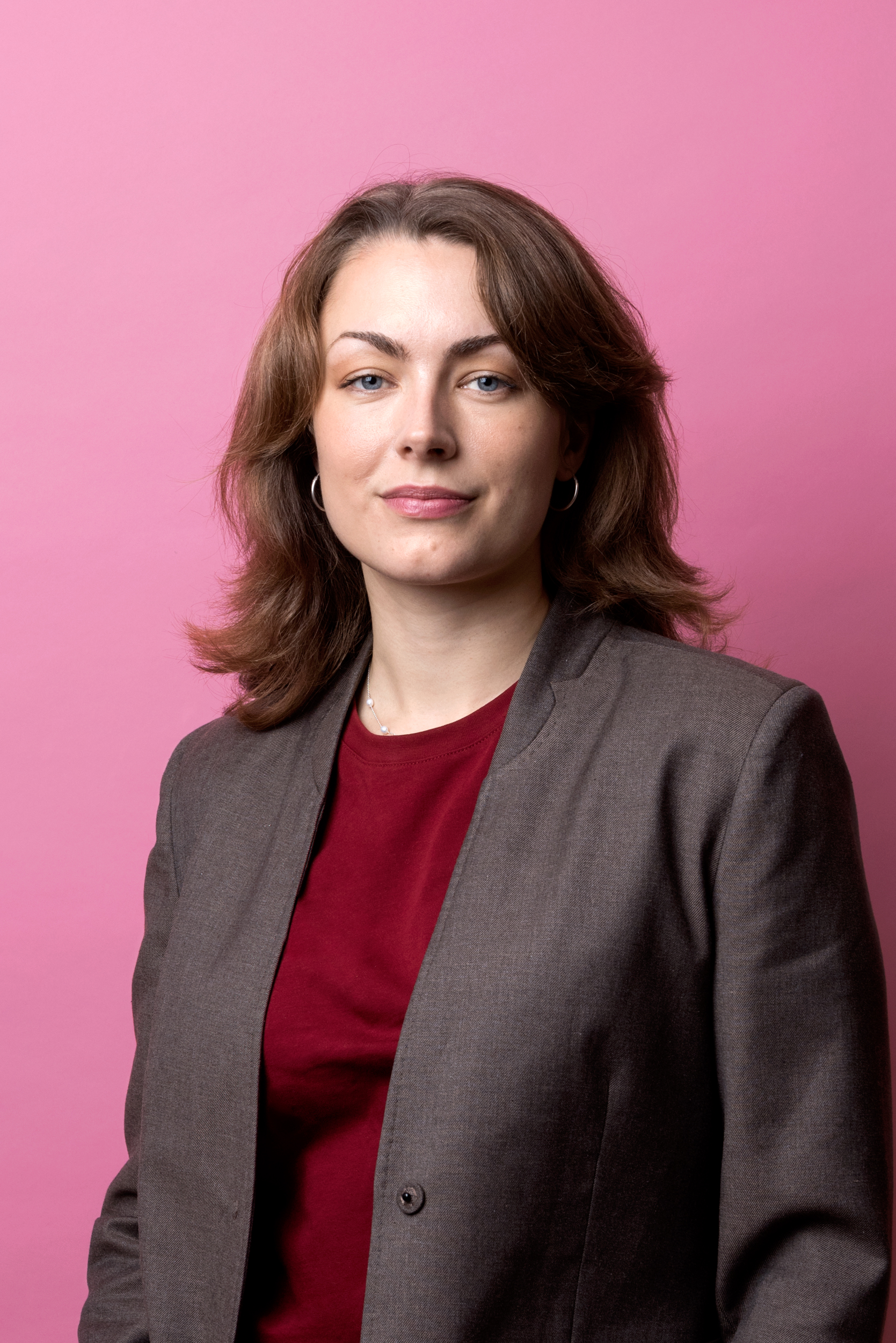 Amanda står vänd lite snett mot kameran. Hon har röd tröja och brun kavaj på sig.