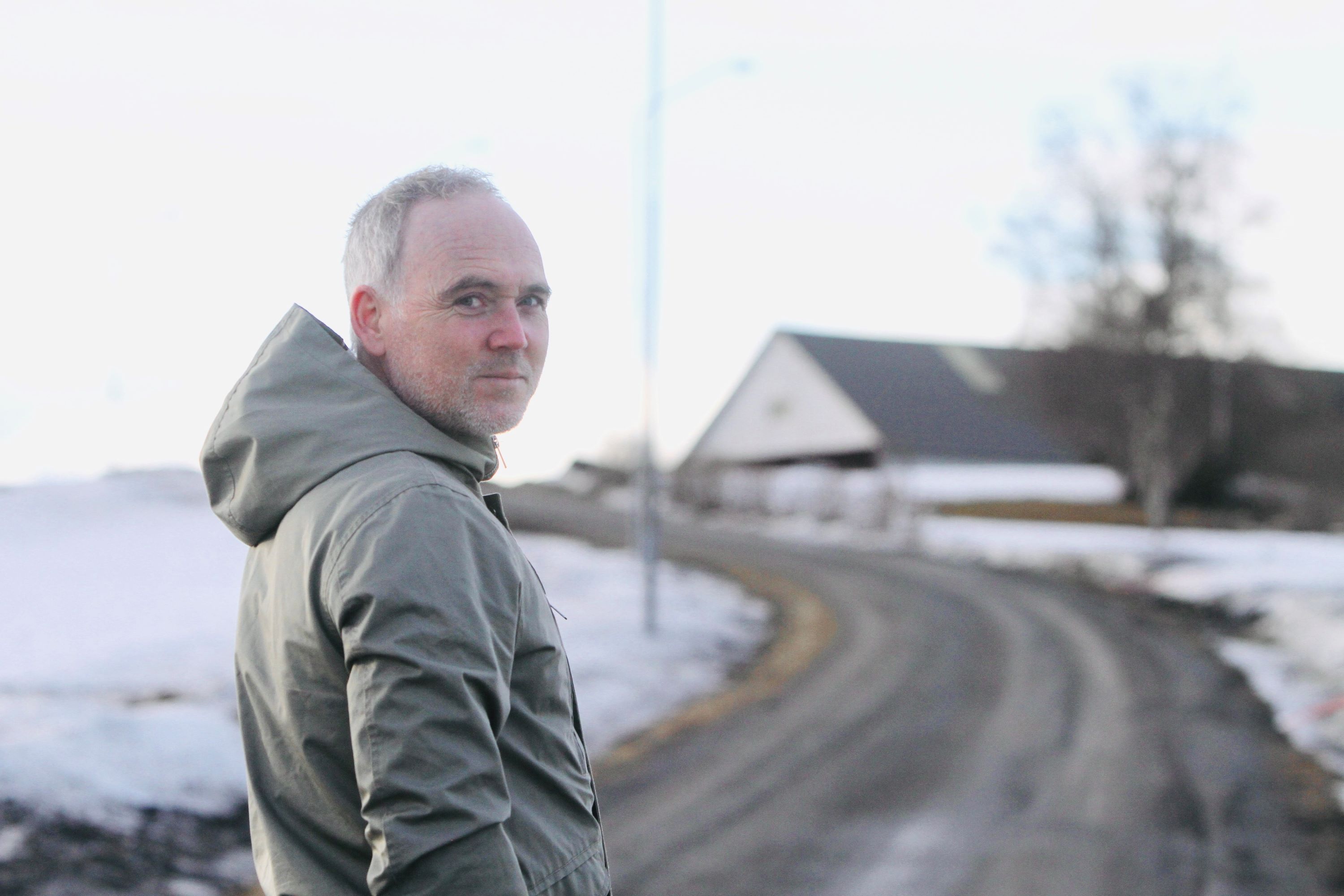 Klas Fritzon står på en landsväg med ett töande vinterlandskap i bakgrunden. Klas har grön parkas och tittar in i kameran.