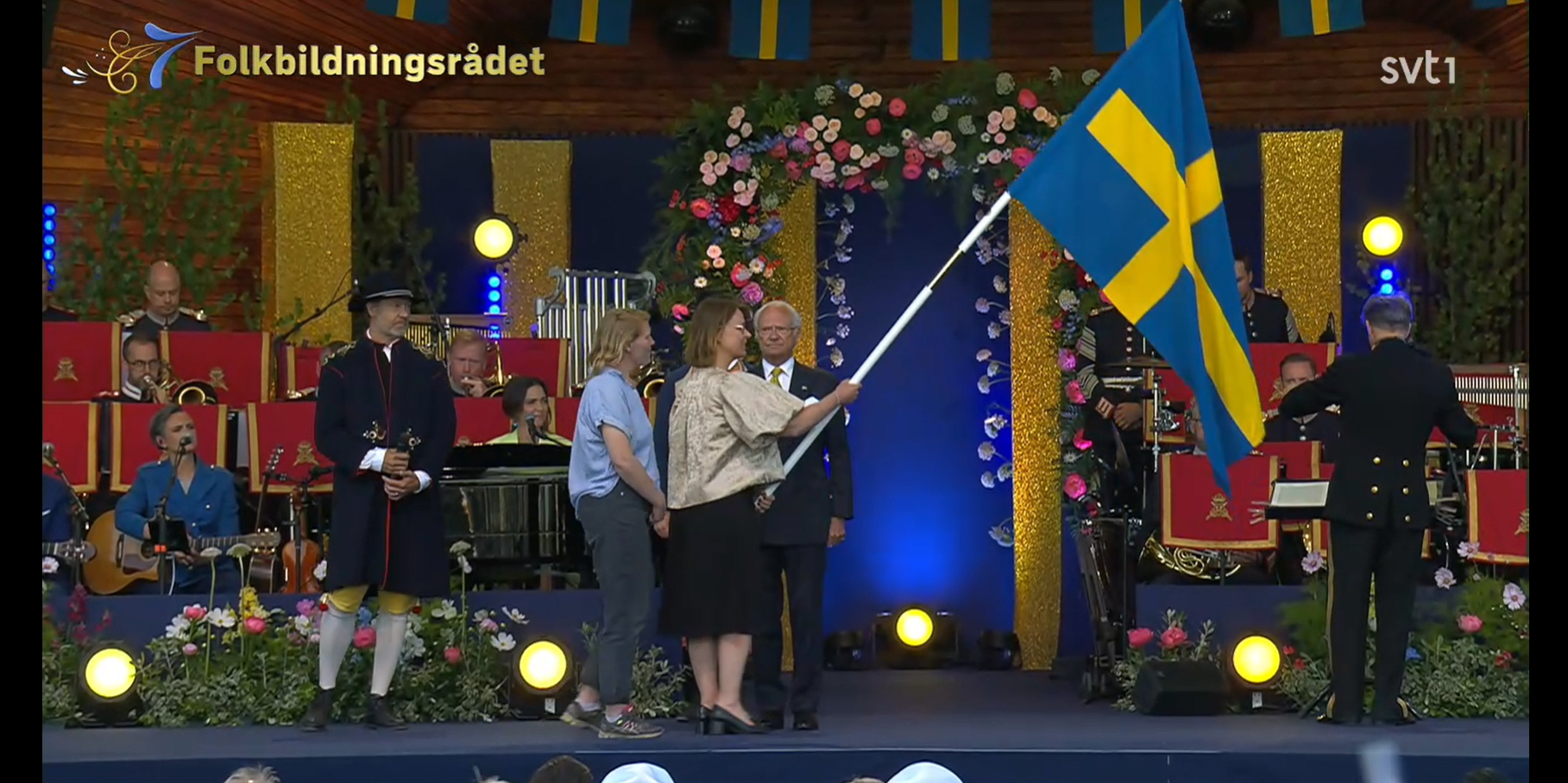 Skärmklipp från tv-sändning. Folkbildningsrådets företrädare har tagit emot en svensk fana från Kungen.