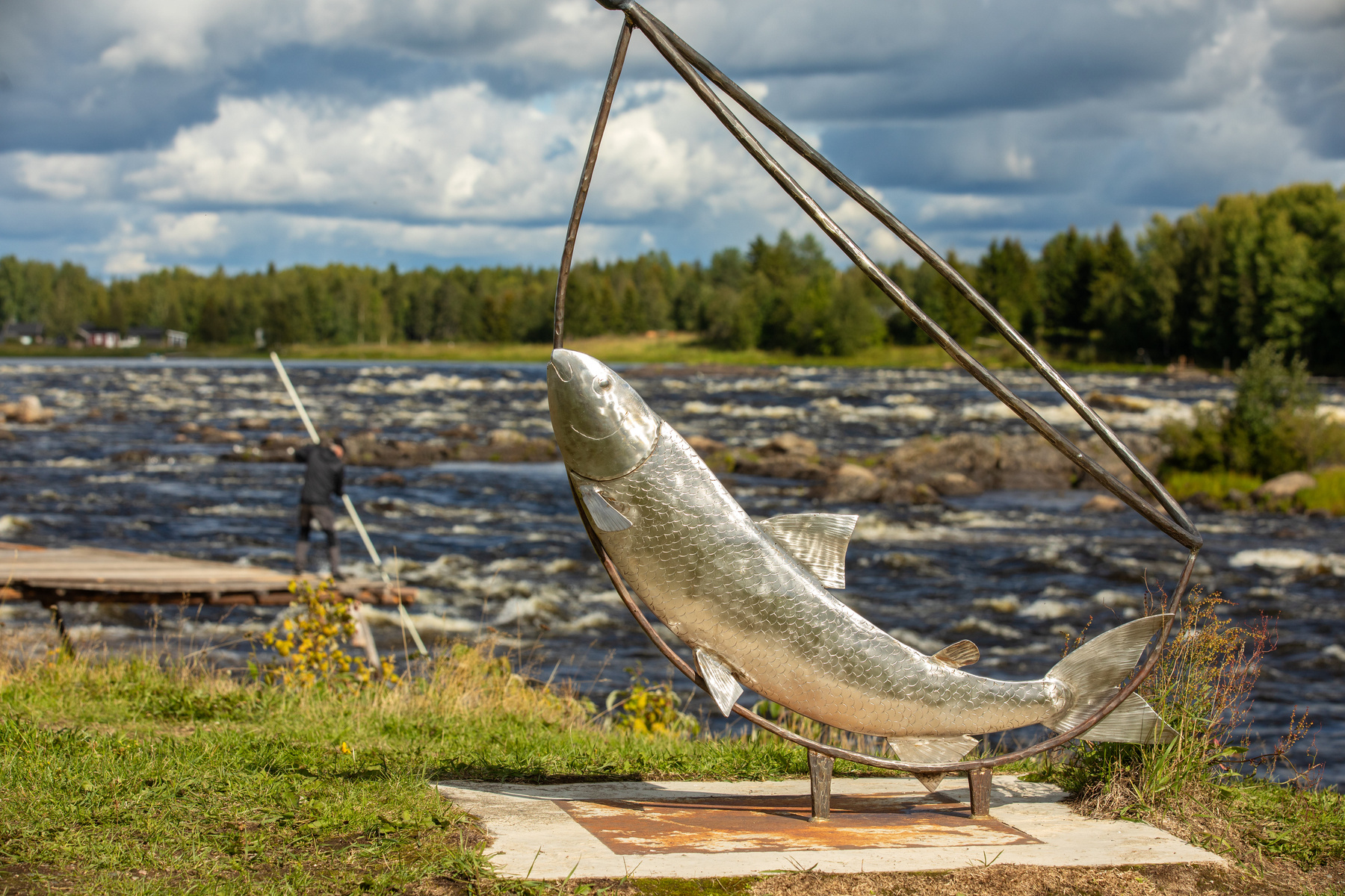 En fisk-skulptur i metall framför en fors.
