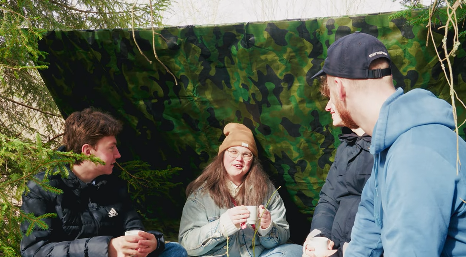 En grupp deltagare sitter i ett vindskydd i skogen och pratar.
