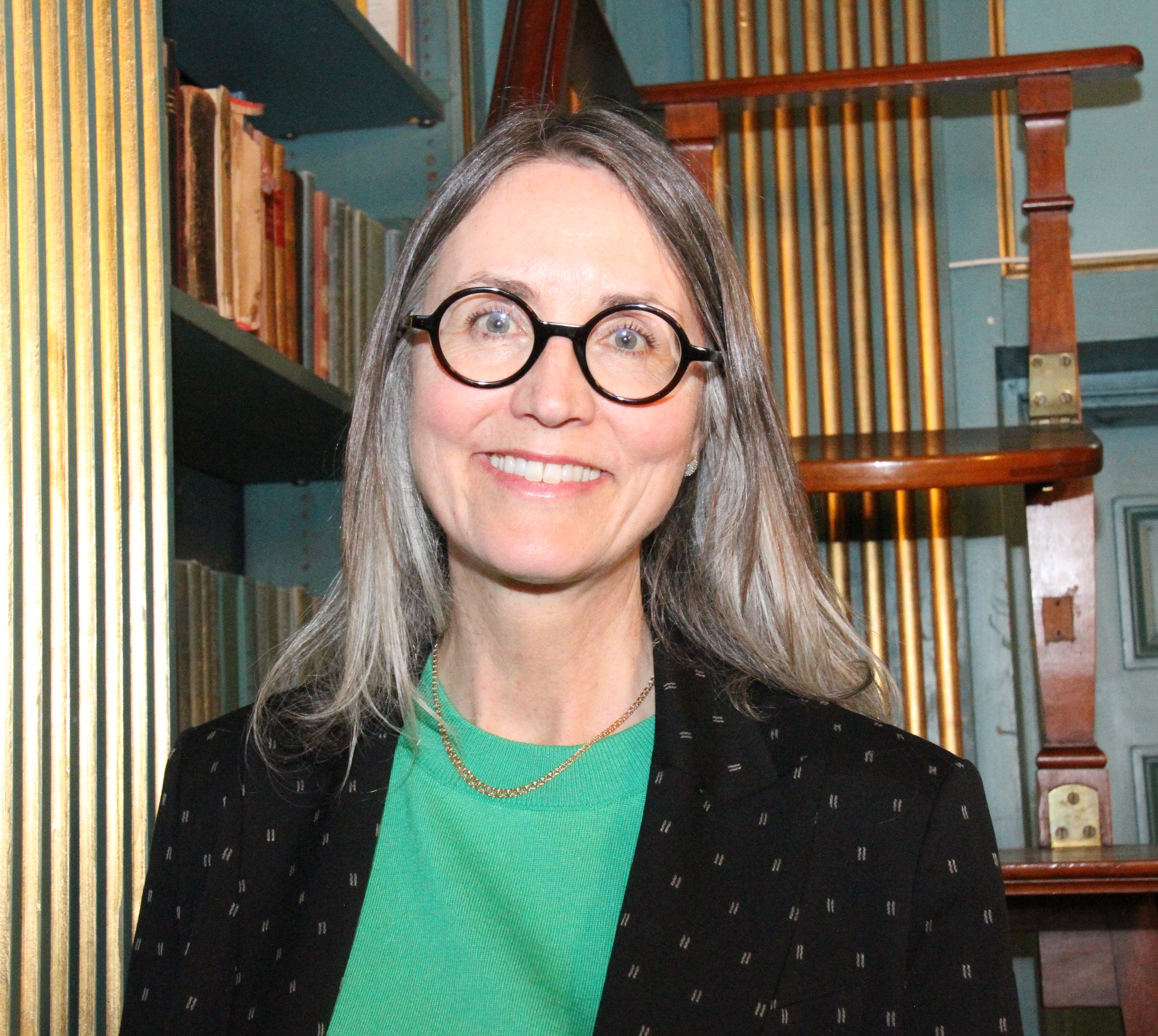 Cecilia står framför några bokhyllor, hon ler stort rakt in i kameran.