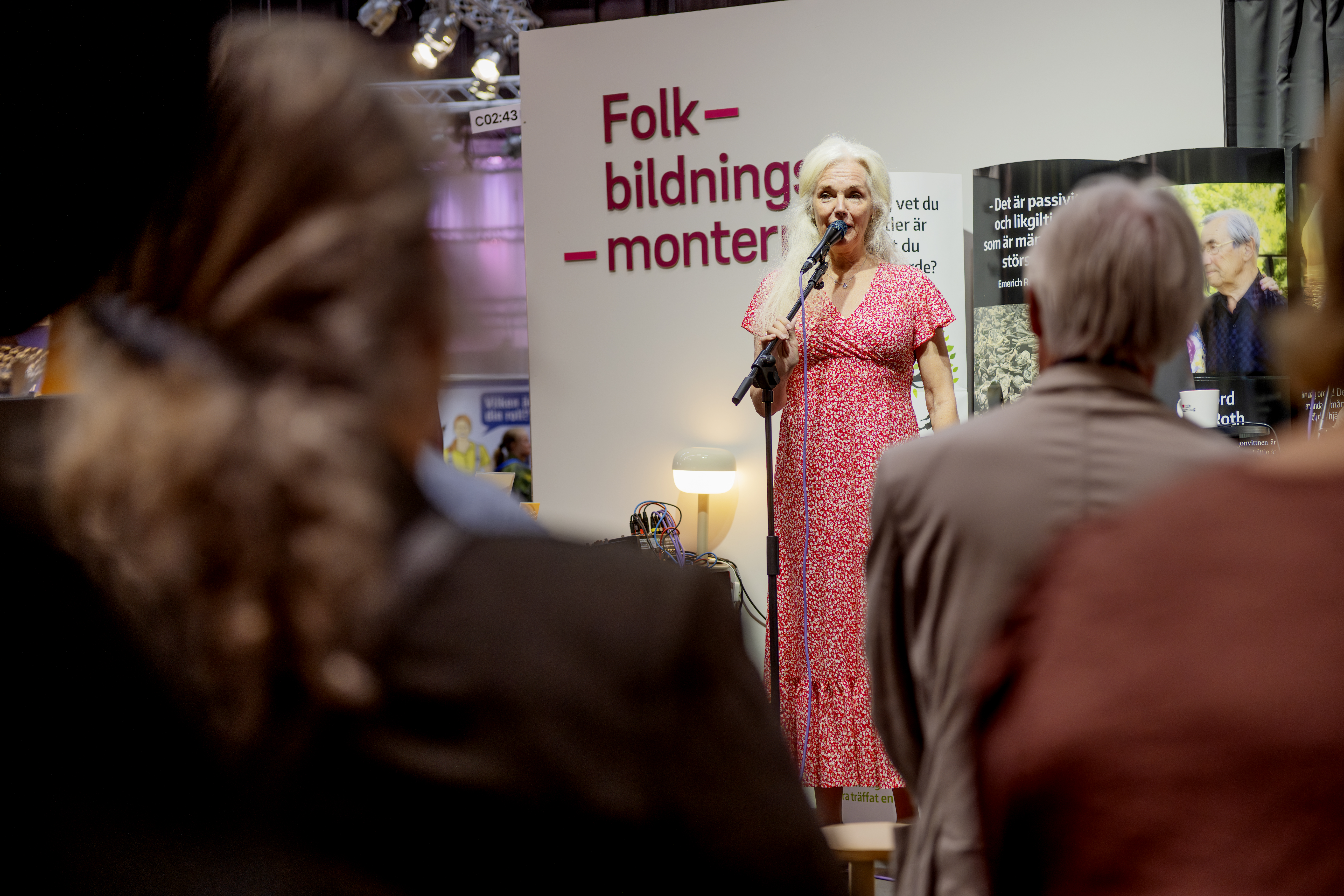 En äldre kvinna håller ett anförande. I bakgrunden står en skärm med texten "folkbildningsmontern".