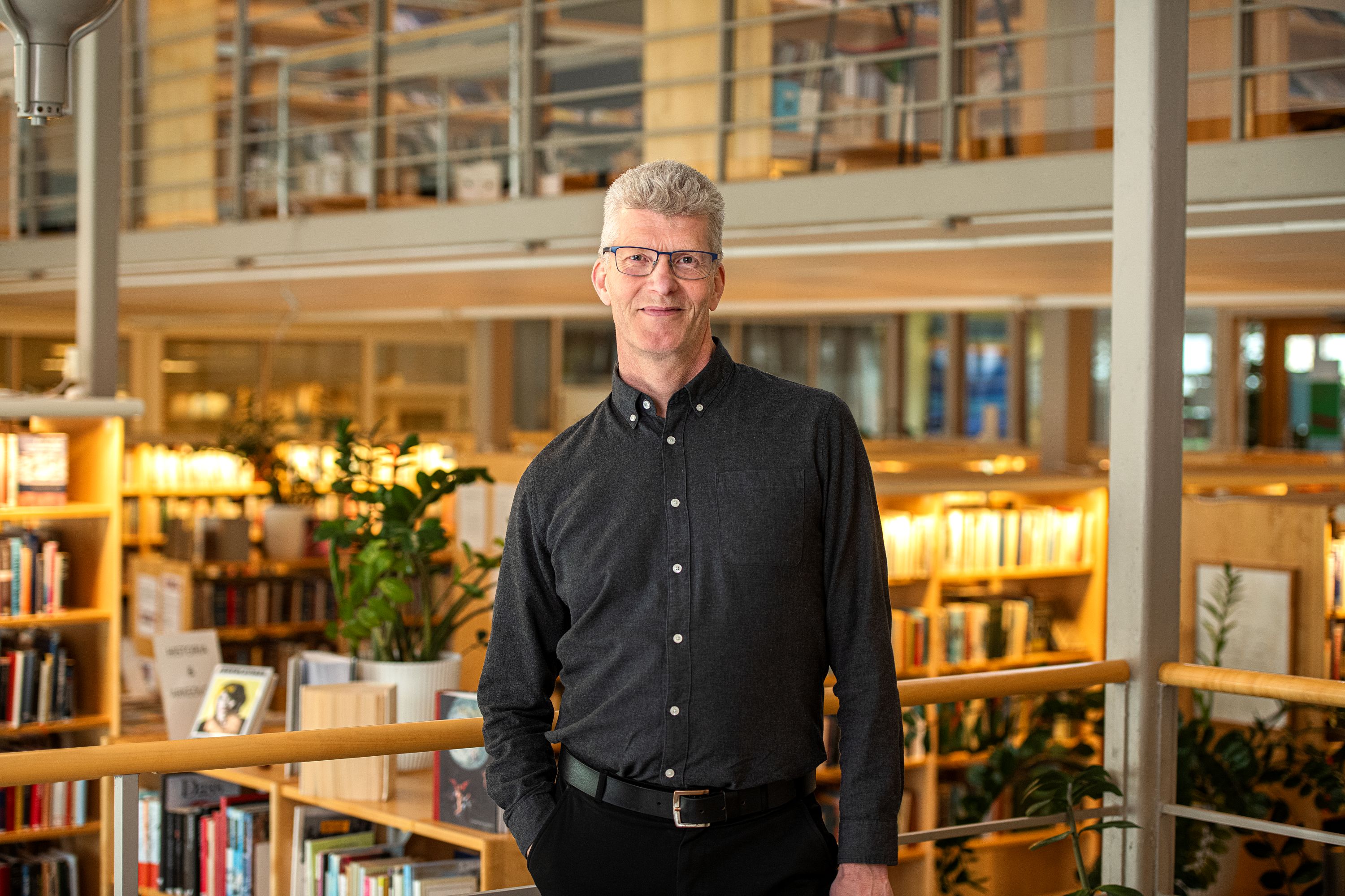 Porträttfoto av Jan Jonsson i bibliotek. Jan ler och är klädd i svart skjorta. 