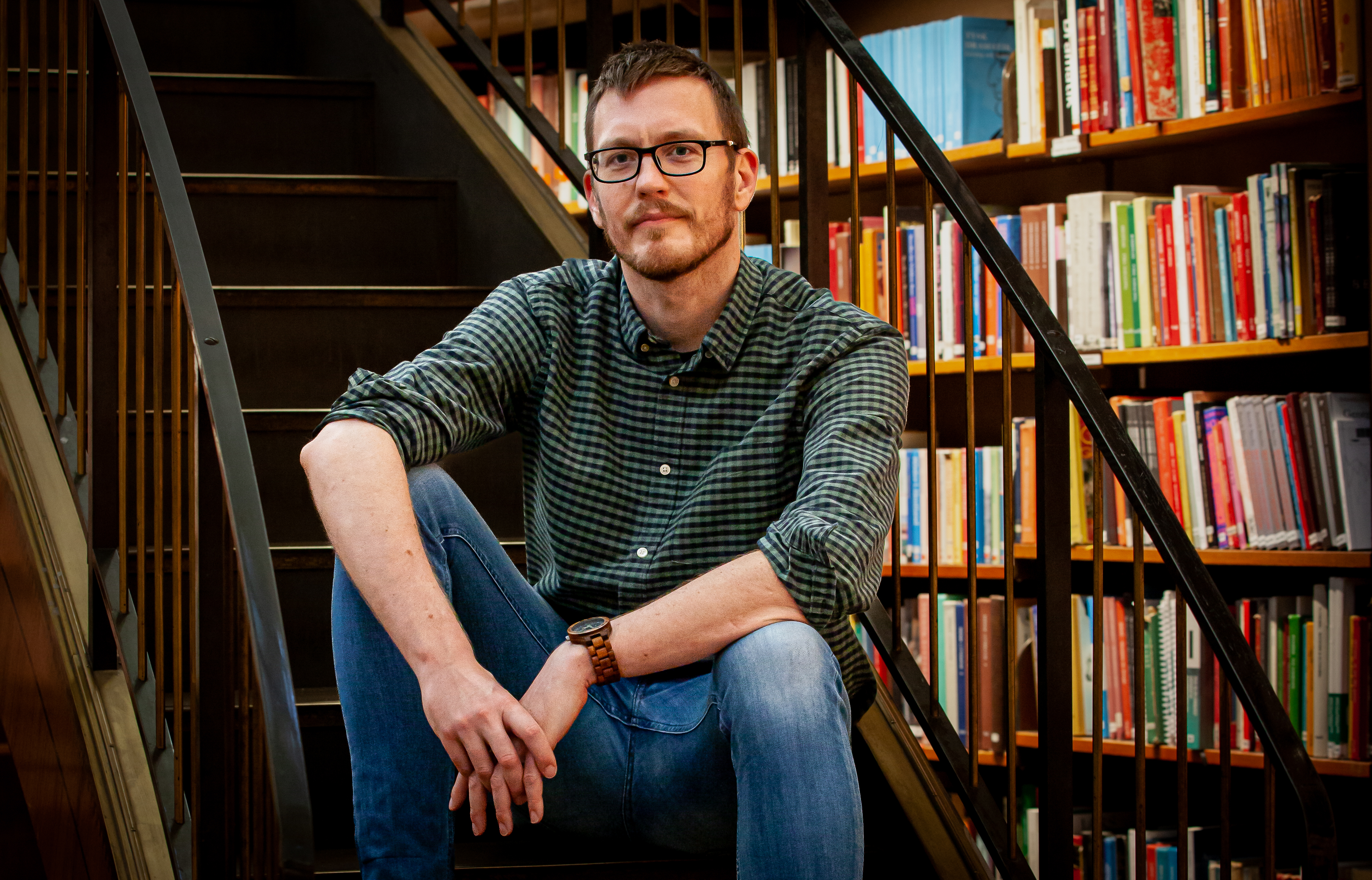 Niklas Hill sitter i en trappa i ett bibliotek, i bakgrunden ser man bokhyllor fyllda med böcker.