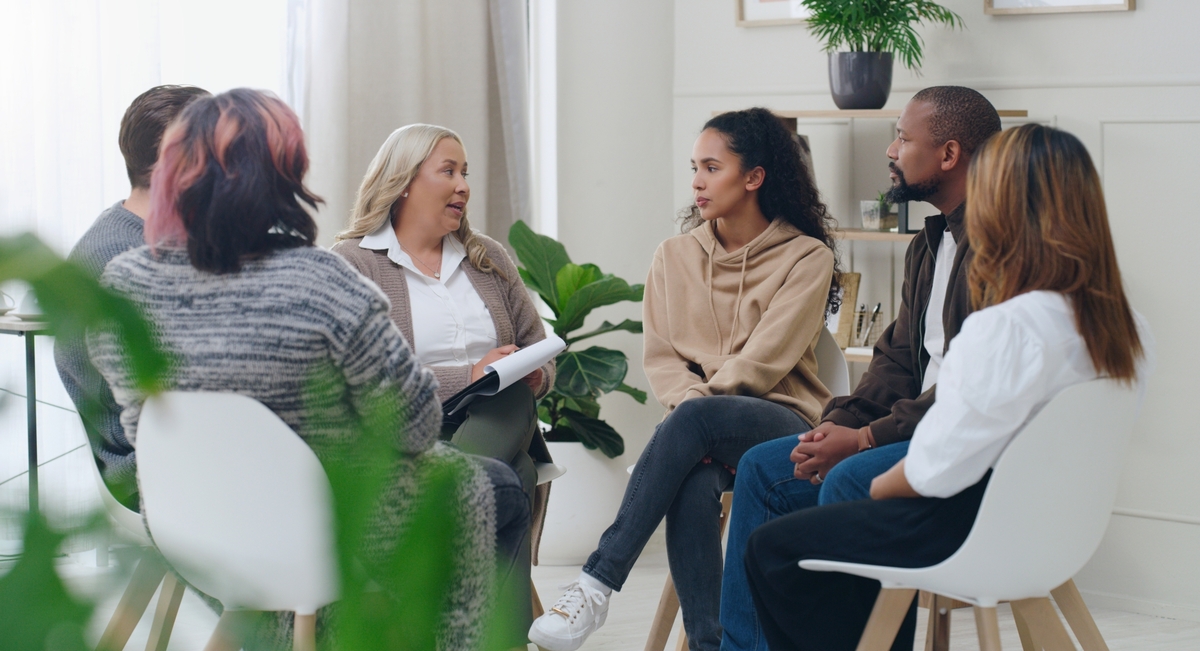 Sex personer sitter på stolar i en ring och samtalar.