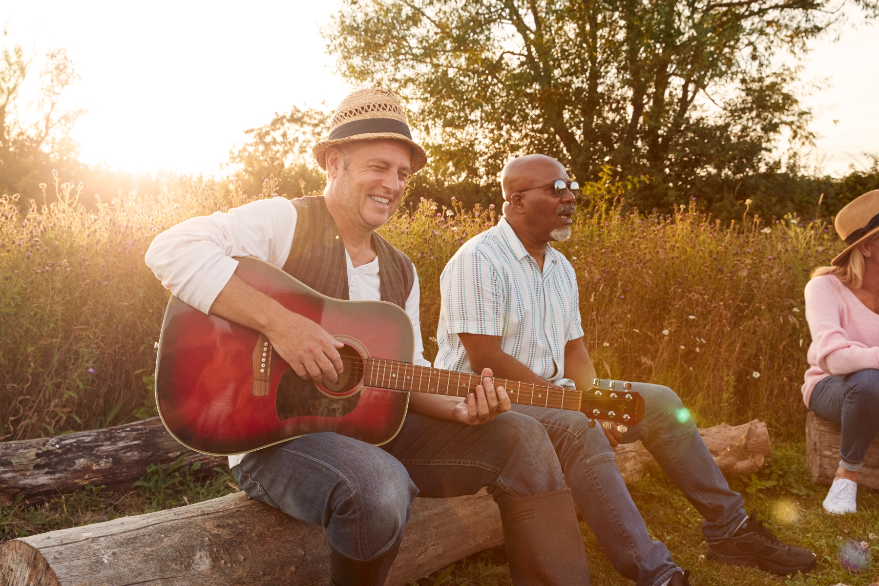 Två äldre män sitter tillsammans utomhus, en av dem spelar gitarr.