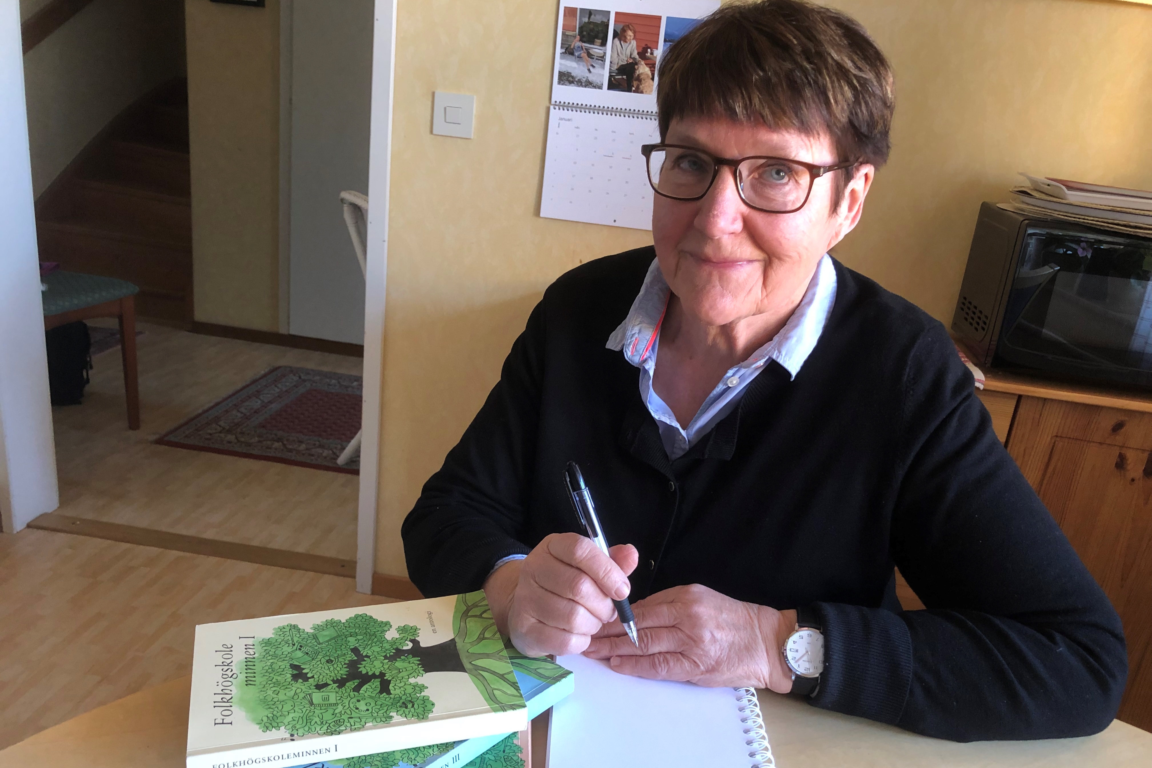 Porträttbild på Signild Håkansson. Signild sitter vid ett bord och signerar sin bok.