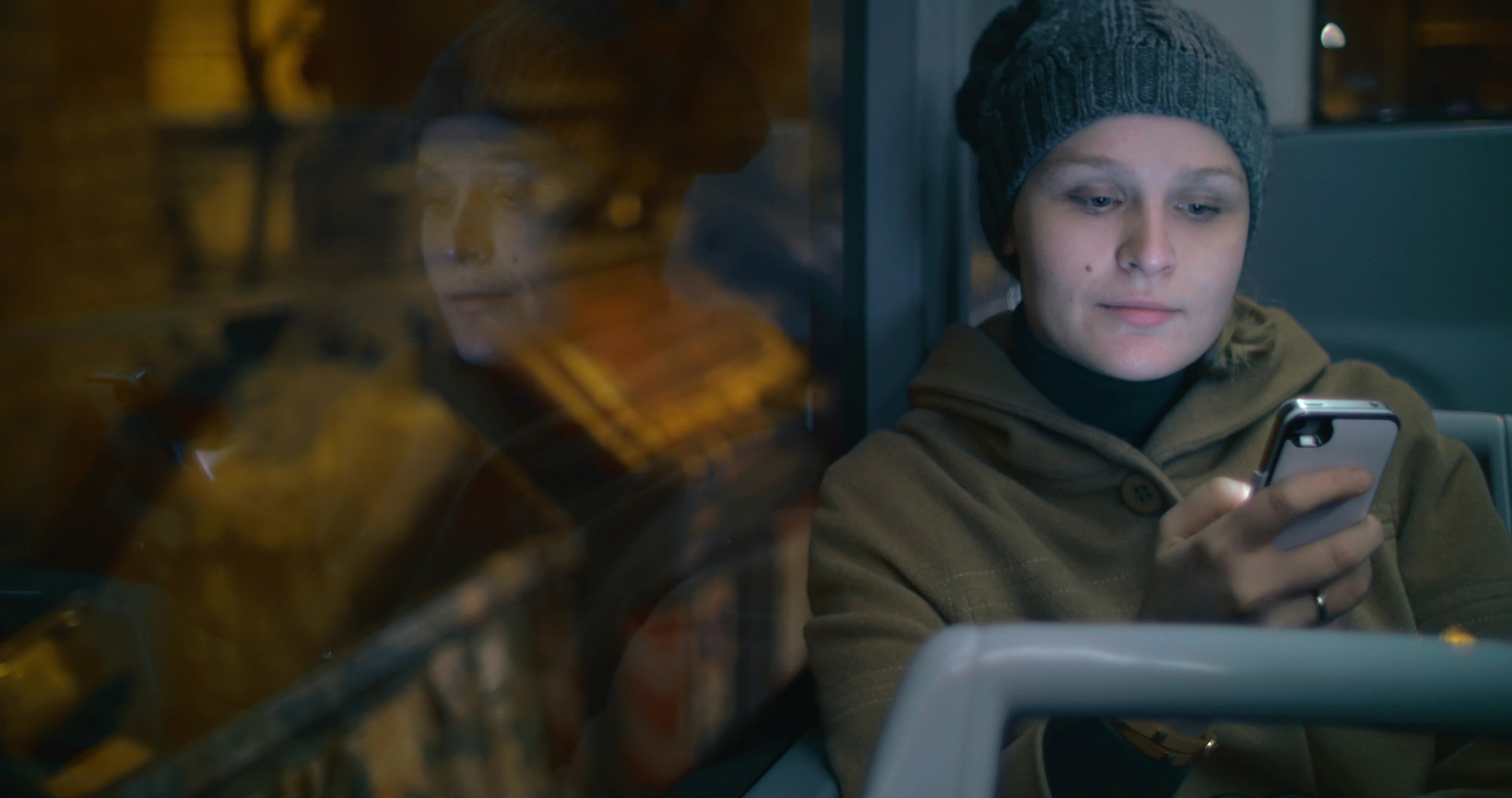 Närbild av kvinna som scrollar på mobilen på bussen. Reflektioner i bussfönstret.