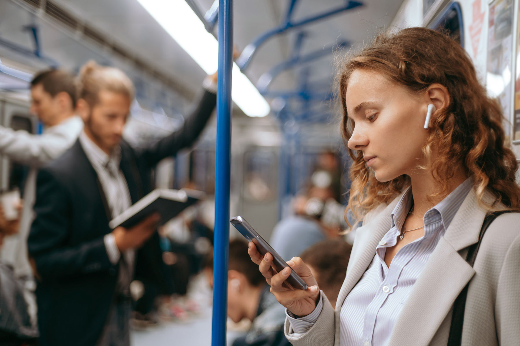 Kvinna med hörlurar läser på sin smartphone i tunnelbanan. Man i bakgrunden läser en bok. Foto: ALBERT YURALAITS